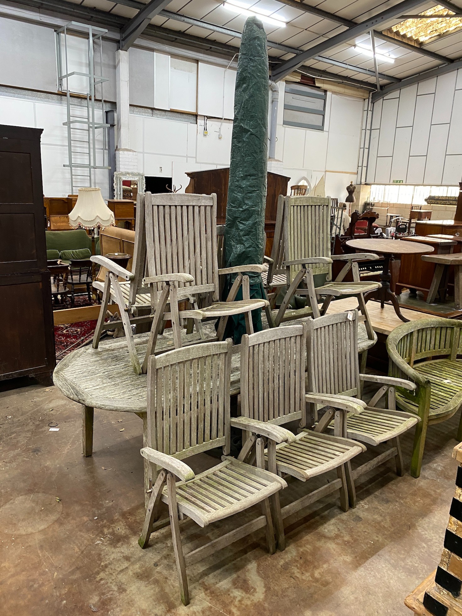 An oval teak garden table, length 260cm, depth 119cm, height 74cm together with eight folding chairs, parasol and cast metal stand.